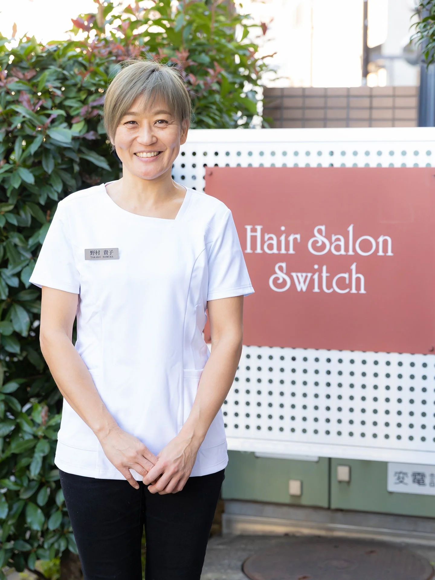 Hair salon Switchの看板の前で微笑む店主 野村 貴子
